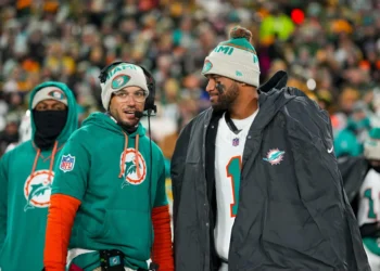 Quarterback Tua Tagovailoa #1 of the Miami Dolphins and head coach Mike McDaniel of the Miami Dolphins stand on the sidelines prior to an NFL football game against the Green Bay Packers, at Lambeau Field in Green Bay, Wisconsin.