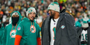 Quarterback Tua Tagovailoa #1 of the Miami Dolphins and head coach Mike McDaniel of the Miami Dolphins stand on the sidelines prior to an NFL football game against the Green Bay Packers, at Lambeau Field in Green Bay, Wisconsin.